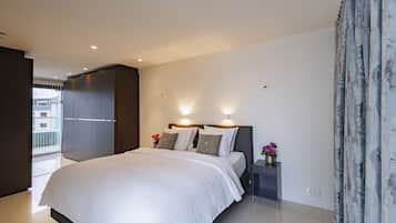 Une chambre moderne avec un grand lit, une armoire, une table de chevet ornée d’un vase de fleurs et une vue sur l’extérieur.