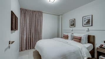 Ein modernes Schlafzimmer mit einem großen Bett, einem Nachttisch, einem an der Wand montierten Fernseher und einem Fenster mit Vorhängen.