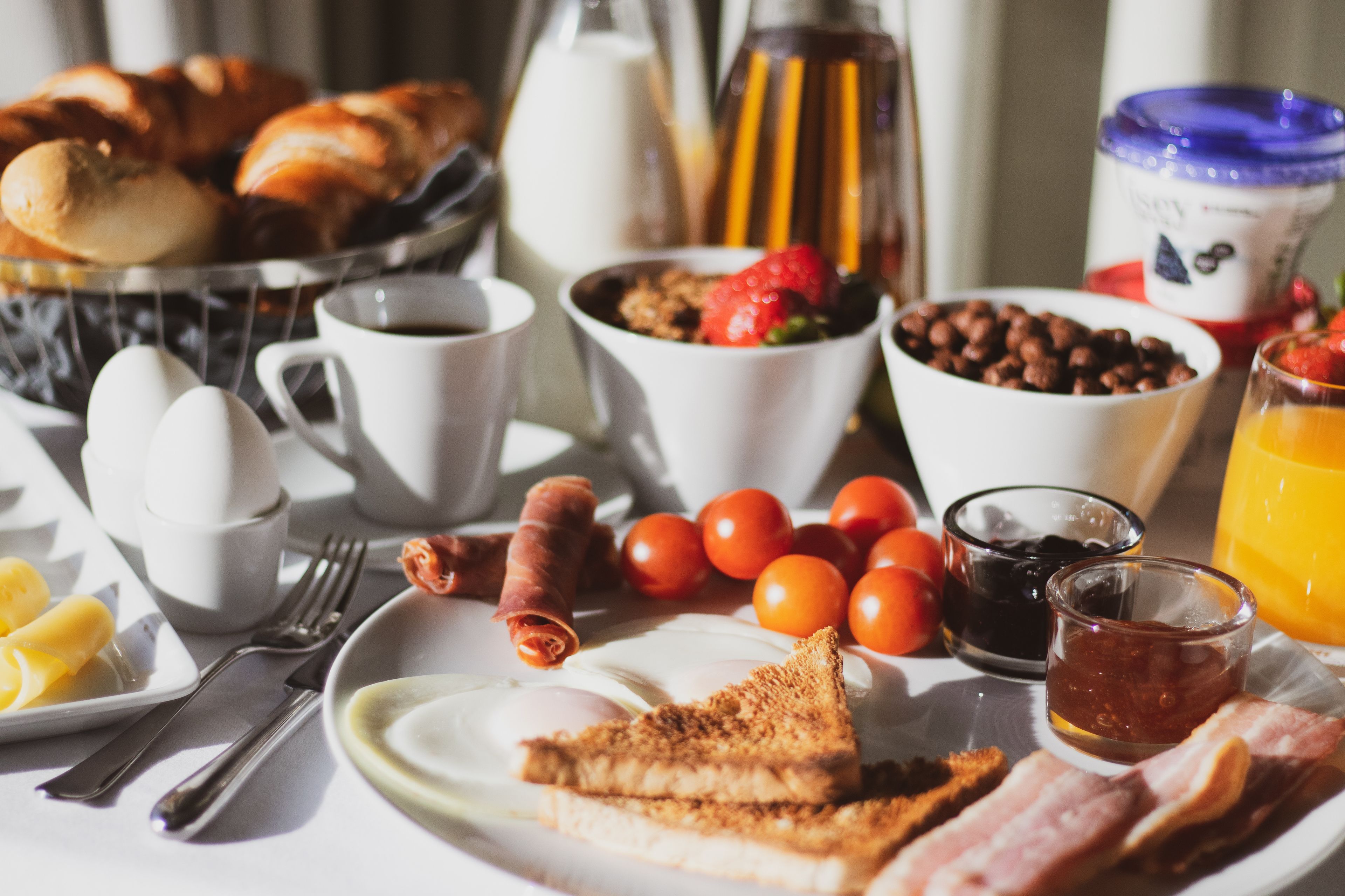 A breakfast table with croissants, eggs, tomatoes, and coffee.