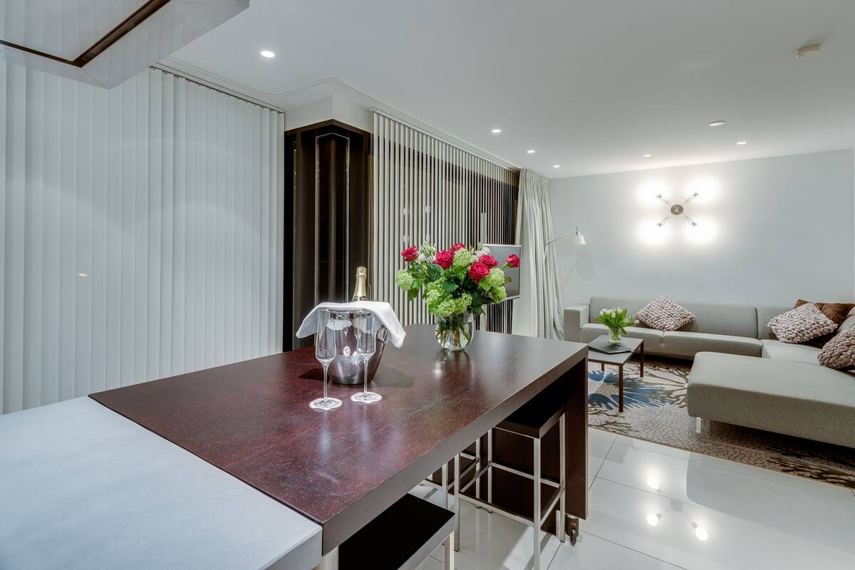 Una sala de estar moderna con comedor, que incluye una mesa de mármol, un conjunto de sofás y un jarrón decorativo con flores.