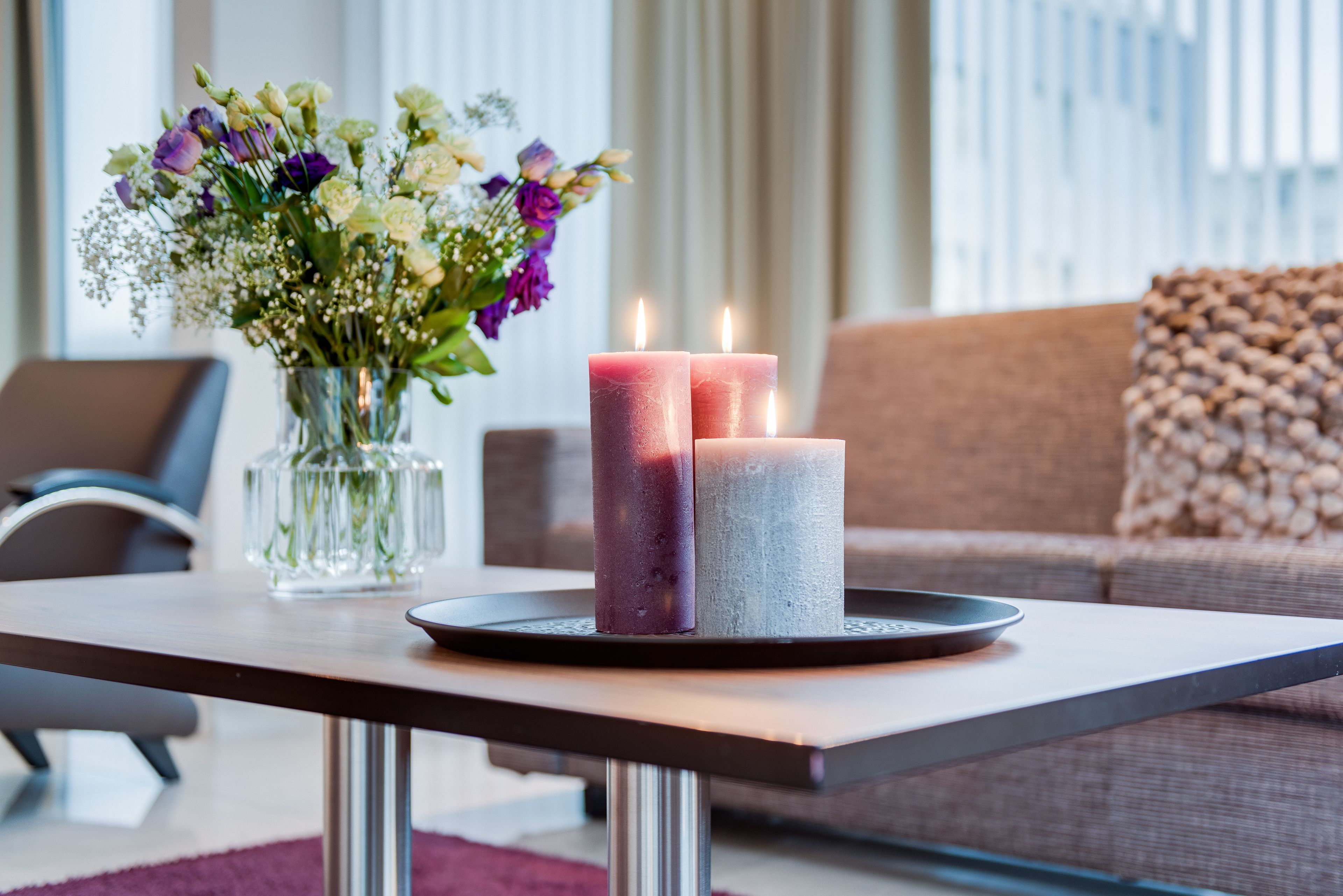Un salon moderne avec un vase en verre rempli de fleurs, deux bougies posées sur un plateau et un canapé agrémenté d’un coussin texturé.
