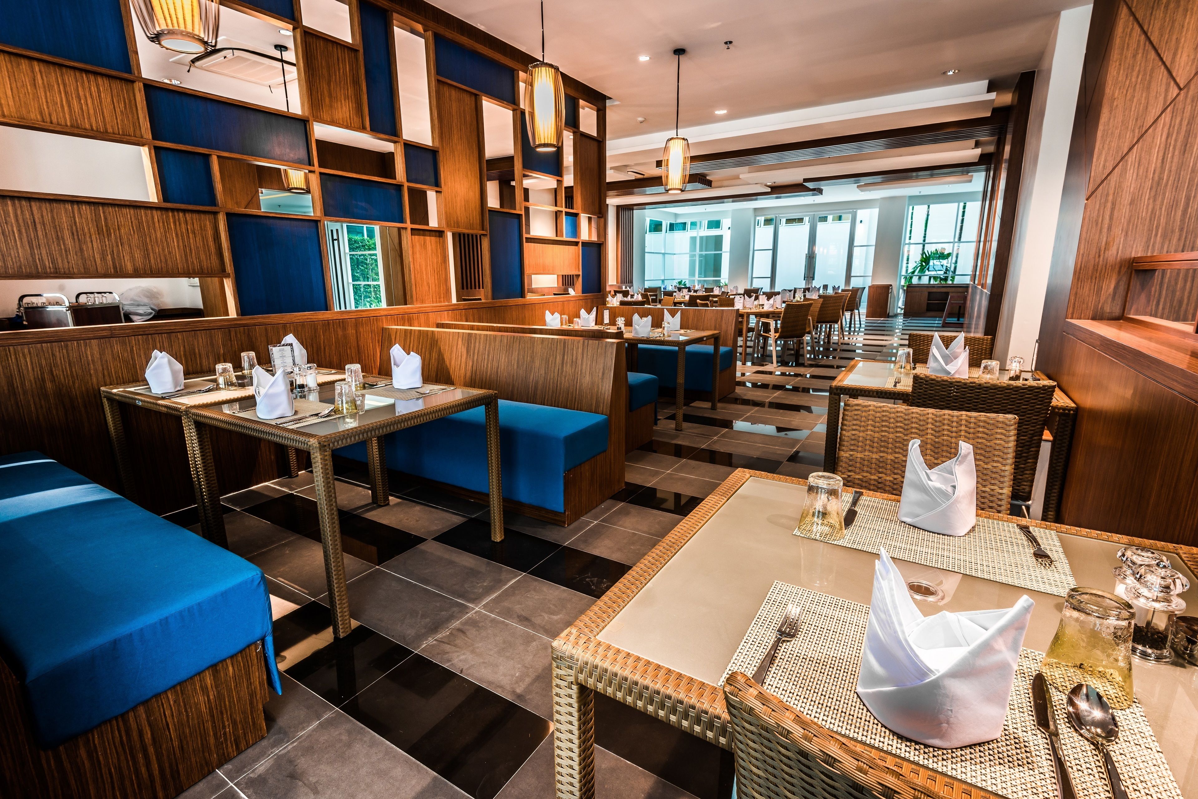 Een restaurant met houten lambrisering, blauwe zitplaatsen en een geruit vloerkleed. Tafels zijn gedekt met witte servetten en bestek.