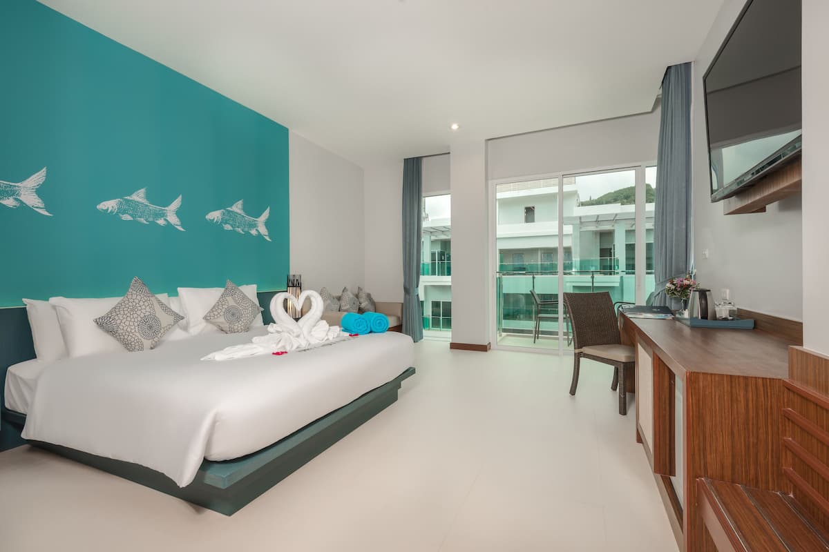 A modern hotel room with a large bed, a desk, and a view of the building's interior.