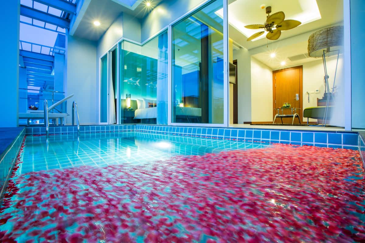 A modern hotel room with a large glass door leading to a swimming pool, a ceiling fan, and a visible bathroom.