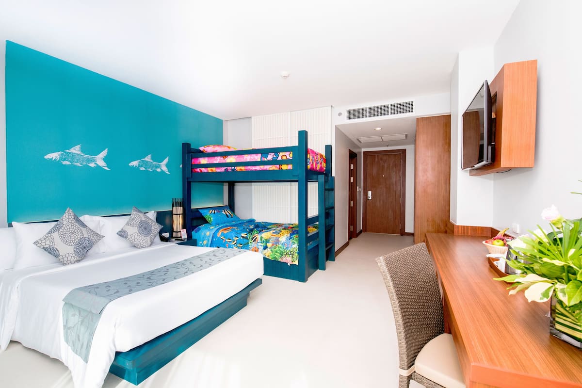A modern hotel room with a bunk bed, a dining area with a wooden table, and a TV mounted on the wall.