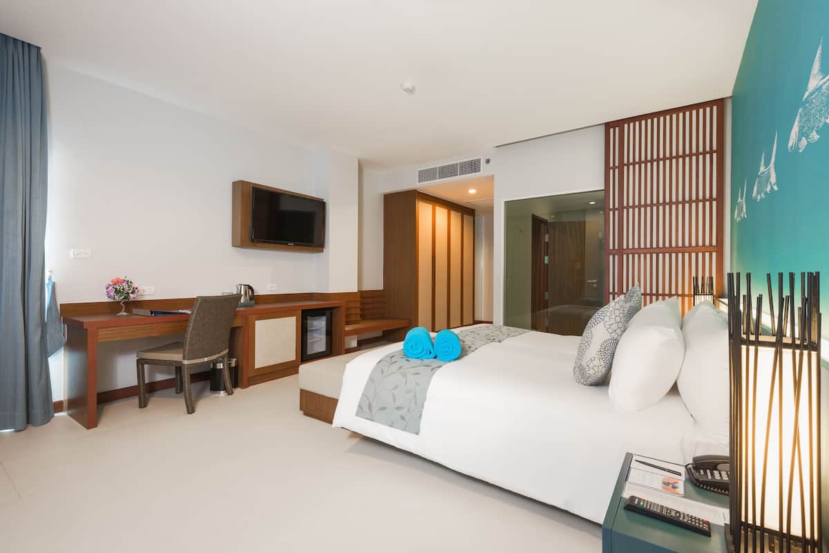 A hotel room with a bed, desk, chair, TV, and a view of the city.
