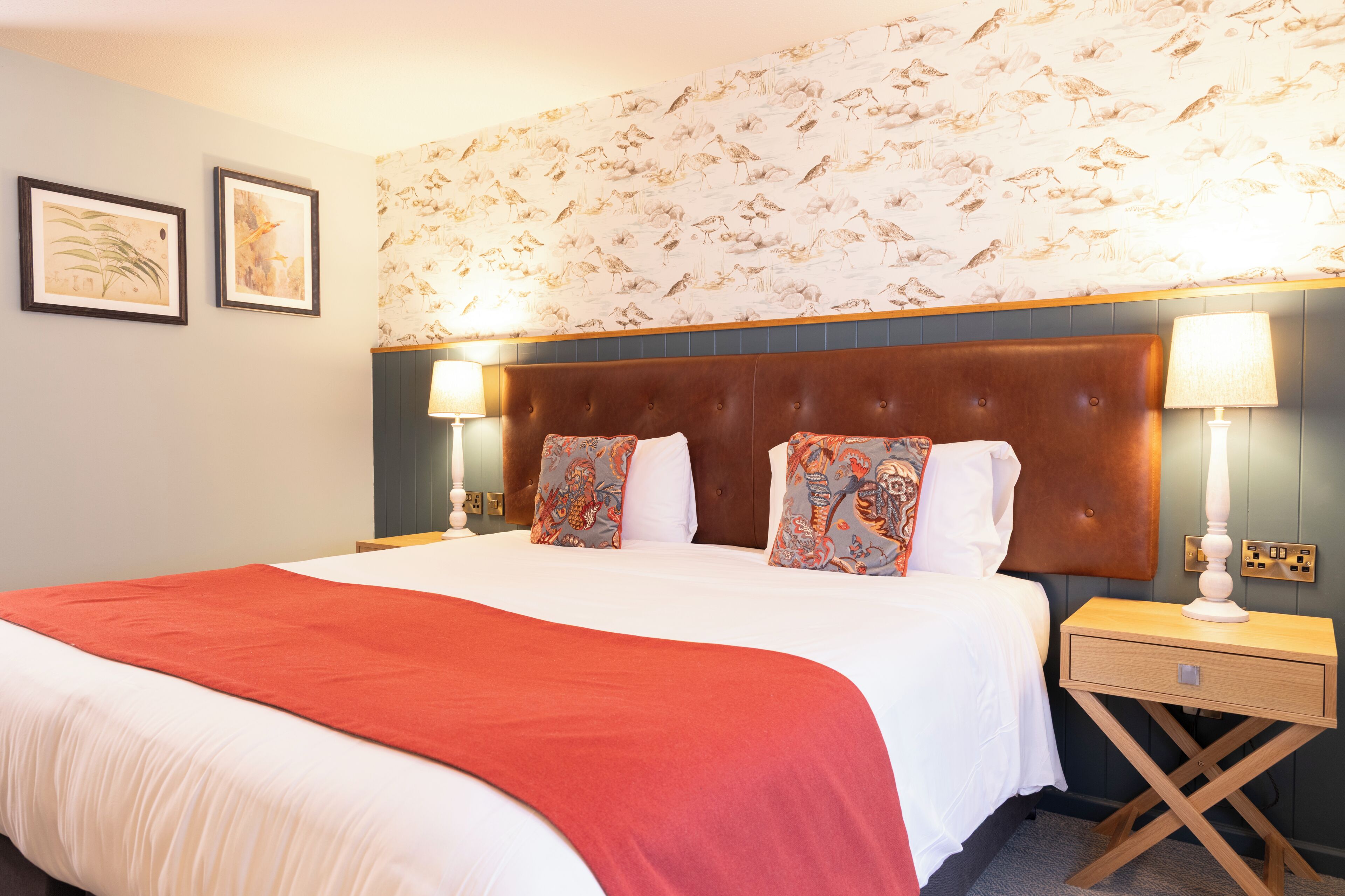 A hotel room with a large bed, two bedside tables, a nightstand, and a wall with bird-patterned wallpaper.