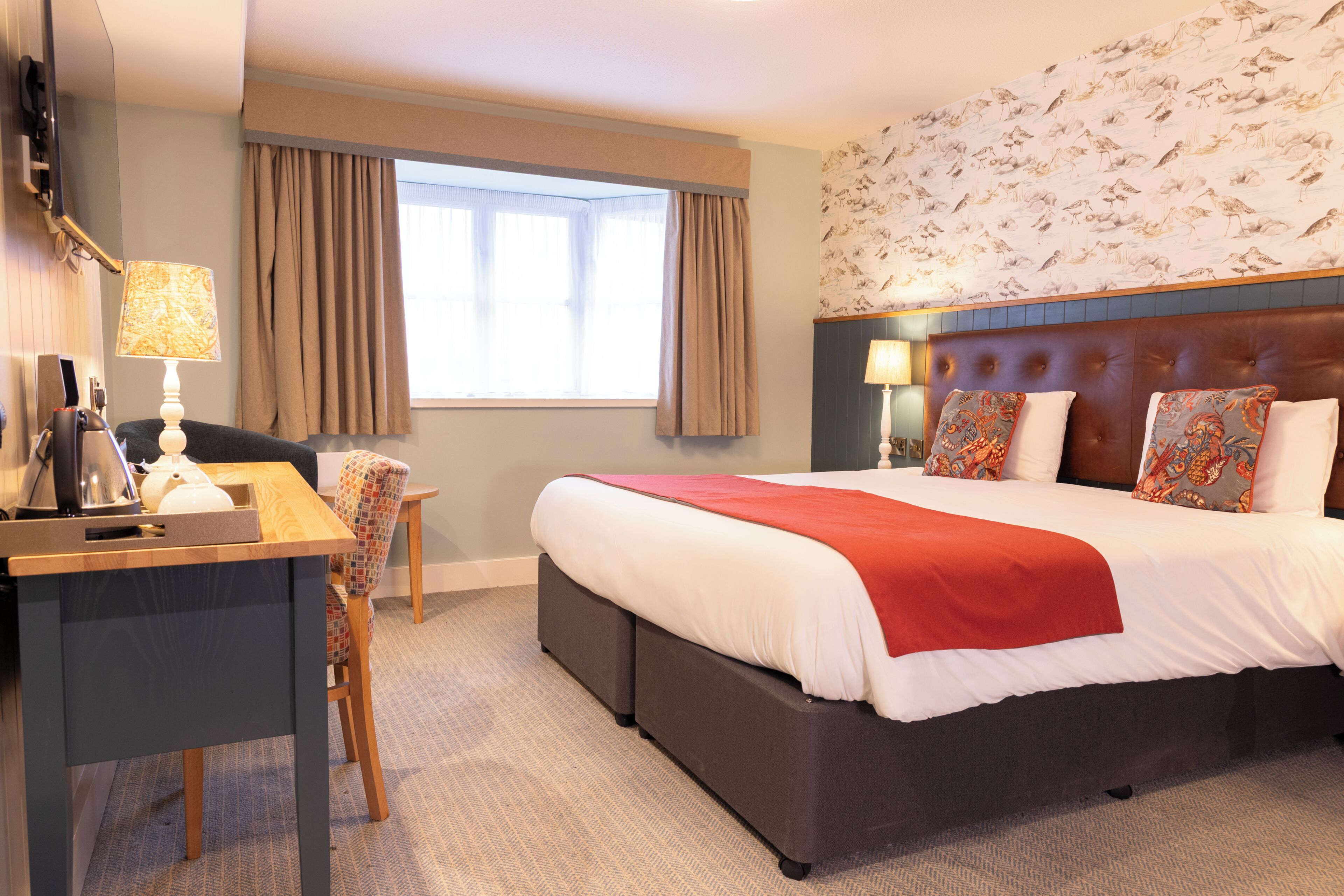 A hotel room with a bed, desk, chair, and a window with curtains.
