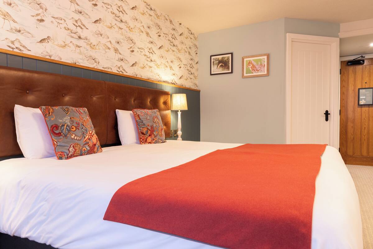 A hotel room with a large bed, a wooden headboard, two wall-mounted lamps, and a door with a wooden panel.