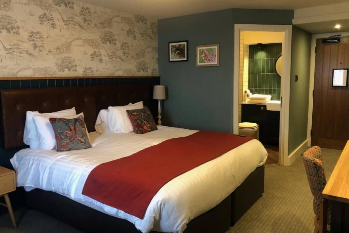 A hotel room with a large bed, a nightstand, a chair, a bathroom with a green wall, and a door.