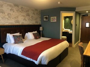 A hotel room with a large bed, a nightstand, a chair, a bathroom with a green wall, and a door.