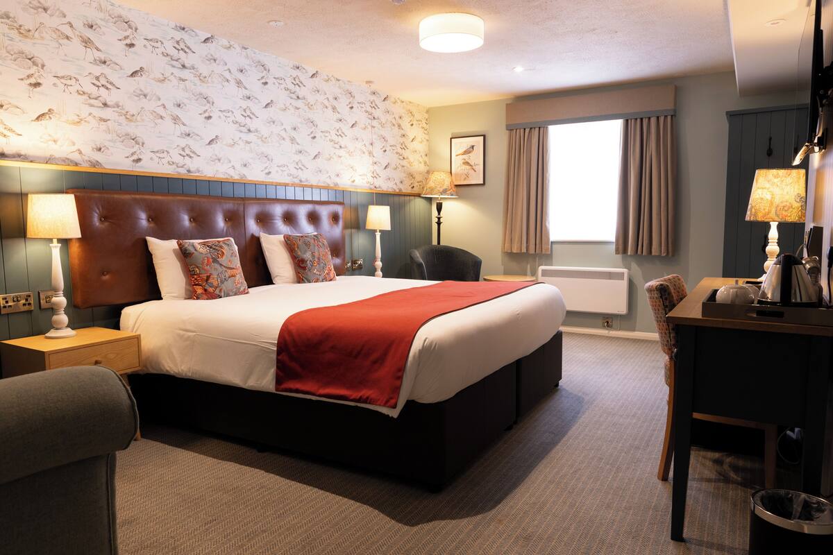 A hotel room with a large bed, two bedside tables, a chair, a desk, and a radiator.