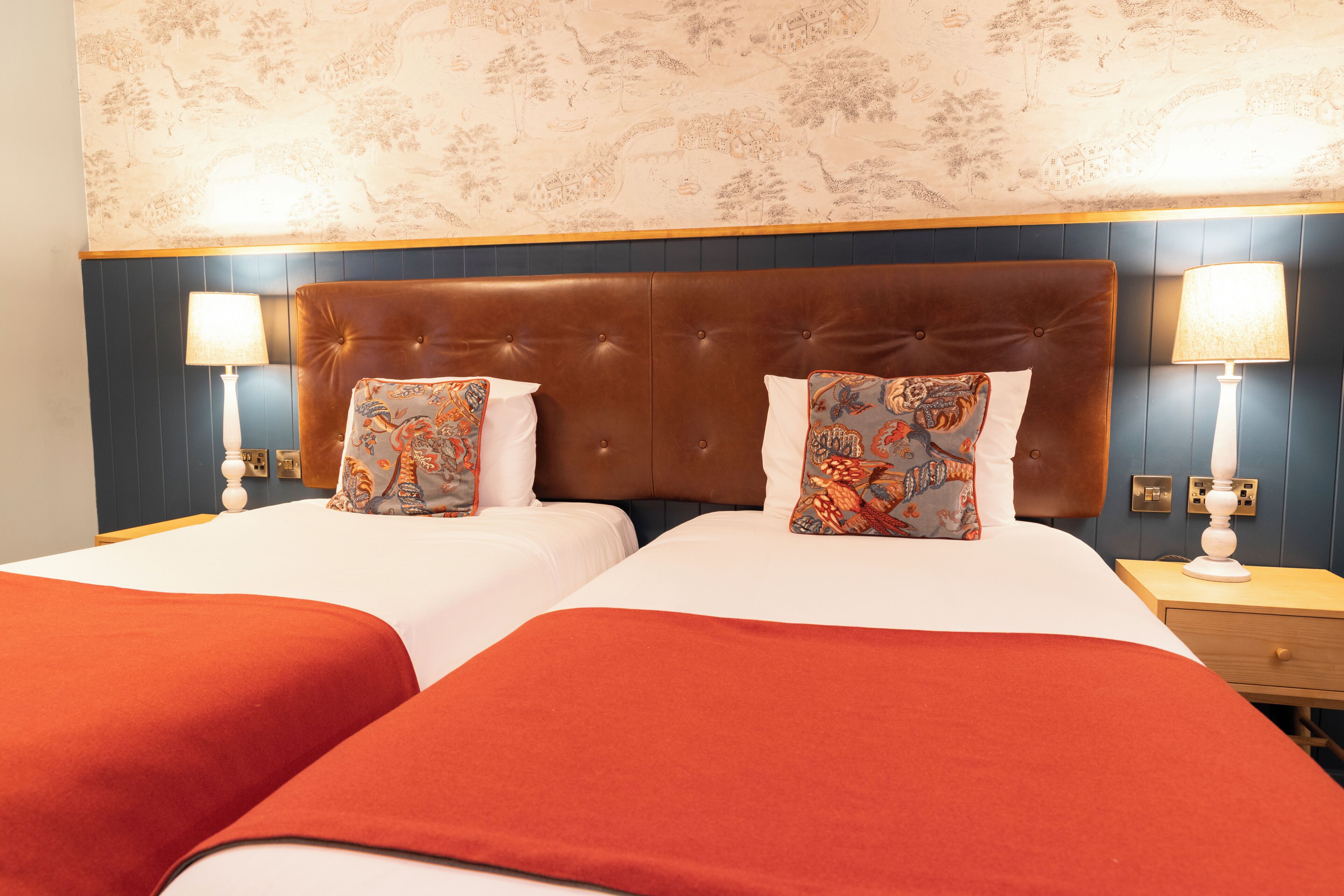 A double bed with a brown headboard, two pillows, a red bedspread, and two bedside lamps.