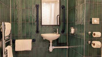 Un baño con lavamanos, espejo, toallero y dispensador de papel higiénico.