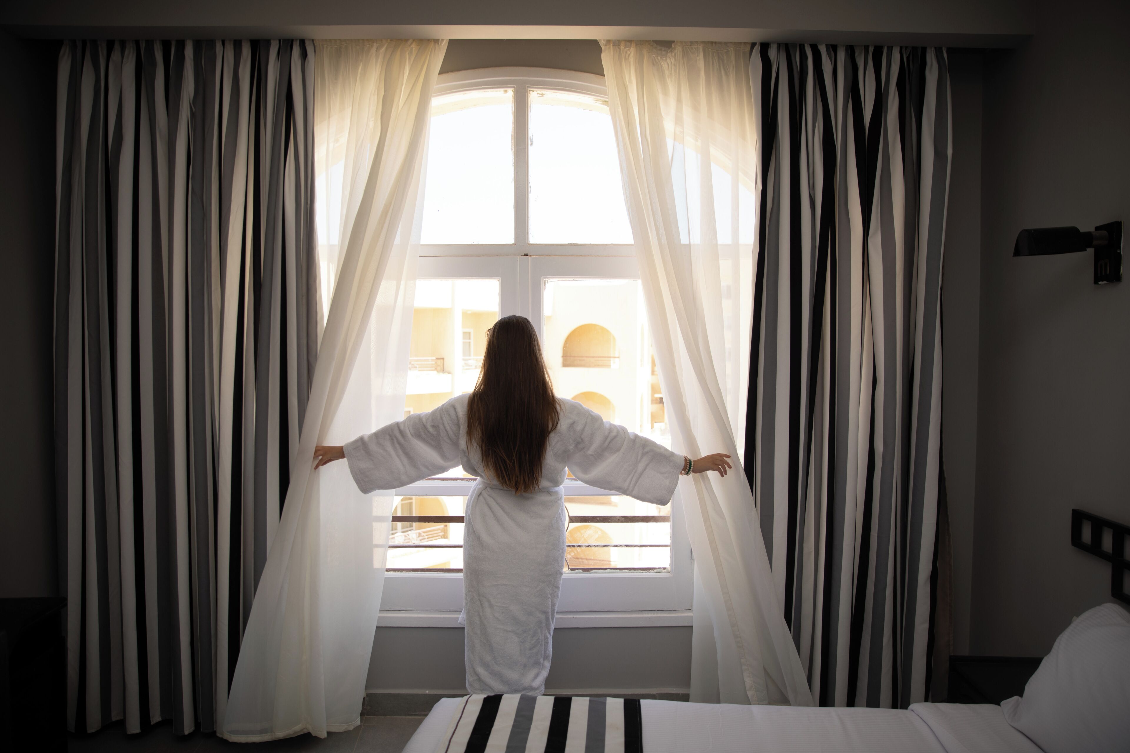 Een kamer met een bed, een raam met gordijnen en uitzicht op een gebouw.