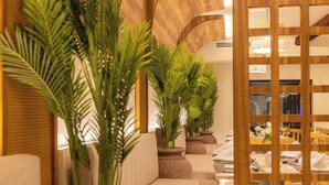Un hall de hotel con áreas de descanso, plantas en macetas y una zona de comedor.