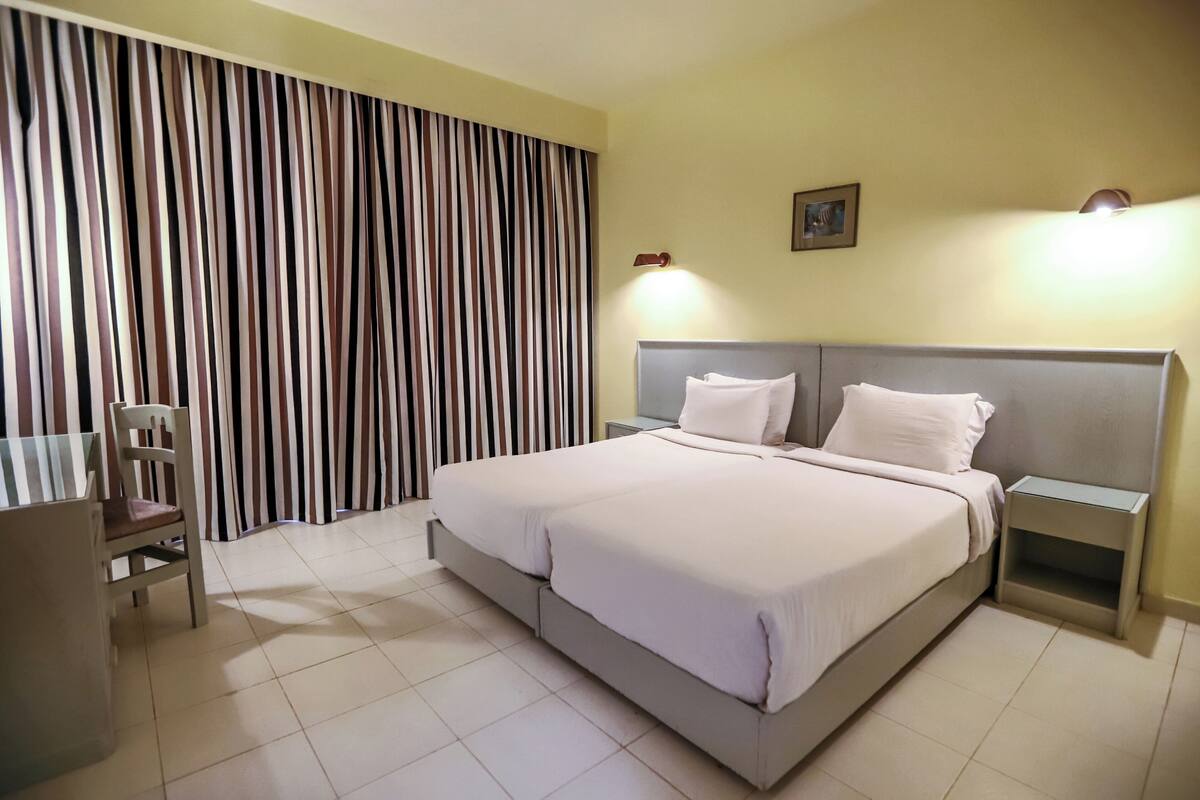 Una habitación de hotel con cama, mesitas de noche, una silla y cortinas.