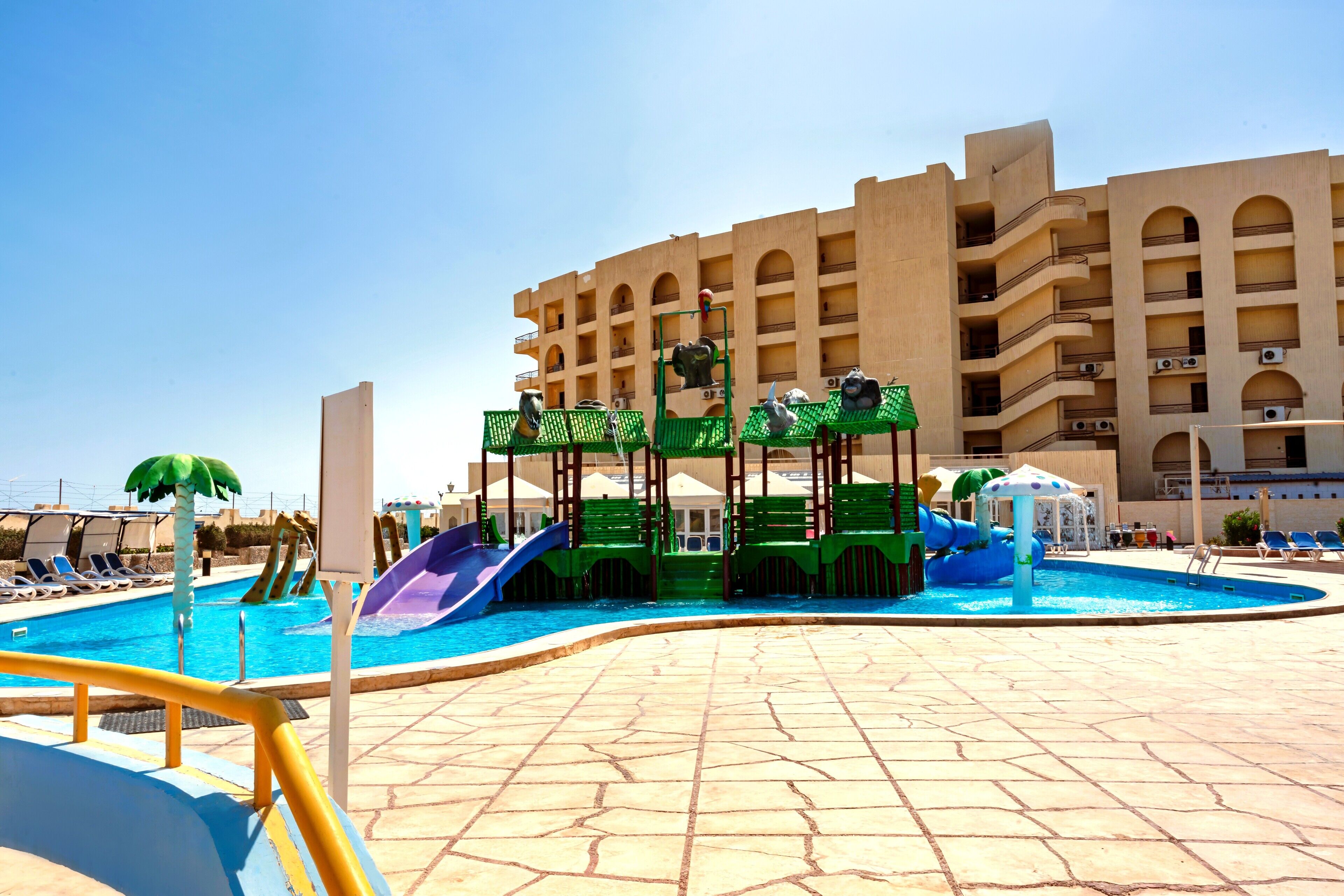 Una piscina con toboganes y zona de juegos acuáticos, rodeada por un edificio con varios balcones.