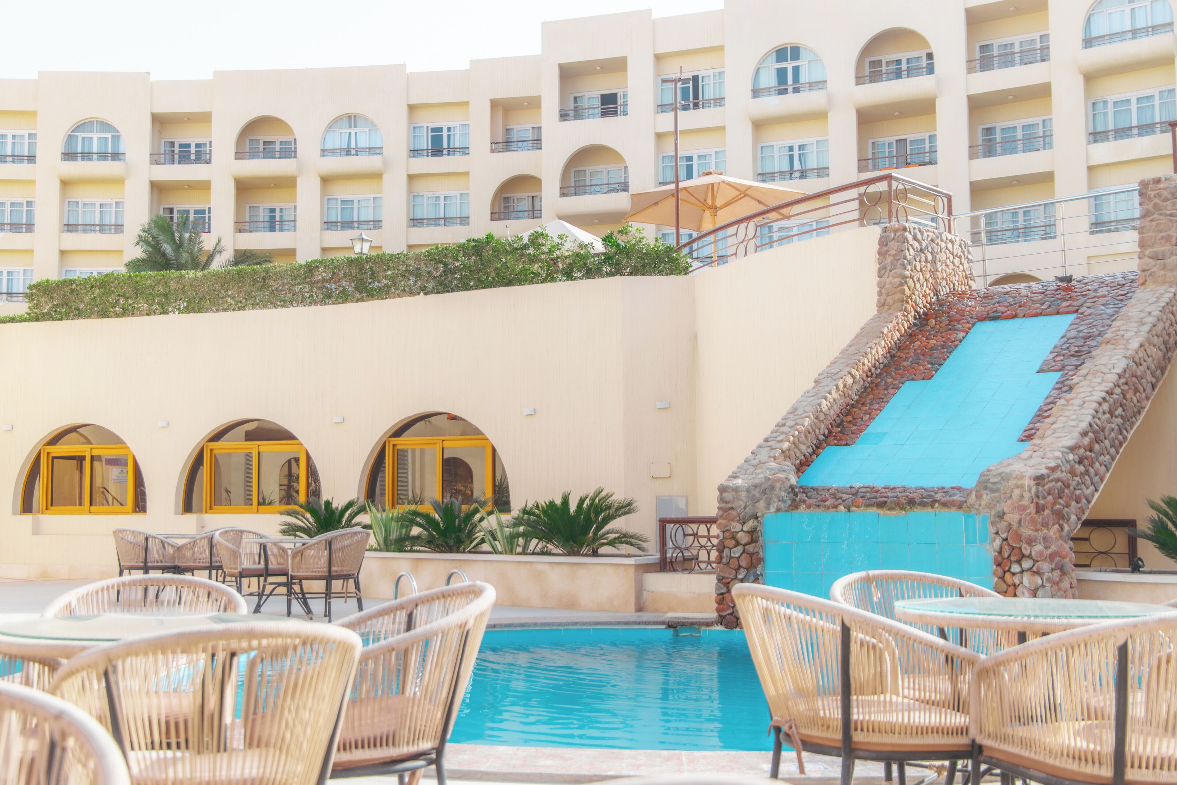 A hotel pool area with wicker chairs, a blue pool, and a stone staircase.