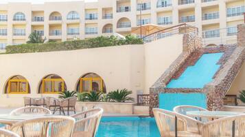 A hotel pool area with wicker chairs, a blue pool, and a stone staircase.