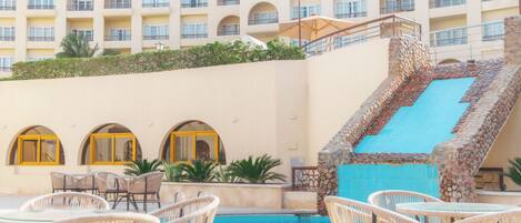 A hotel pool area with wicker chairs, a blue pool, and a stone staircase.