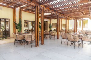 An outdoor cafe area with wicker tables and chairs, wooden pillars, and large windows. - Sunny Days Mirette Family Resort (Hurghada)