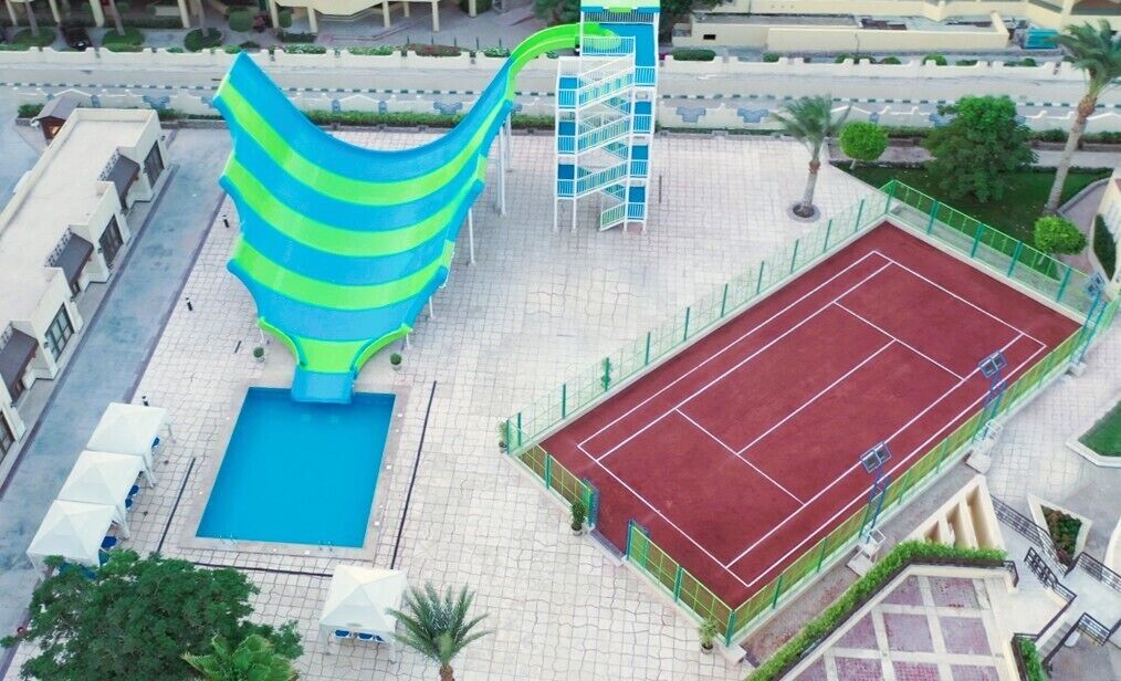 Vista aerea di una struttura sportiva con piscina, campo da tennis e scivolo acquatico.
