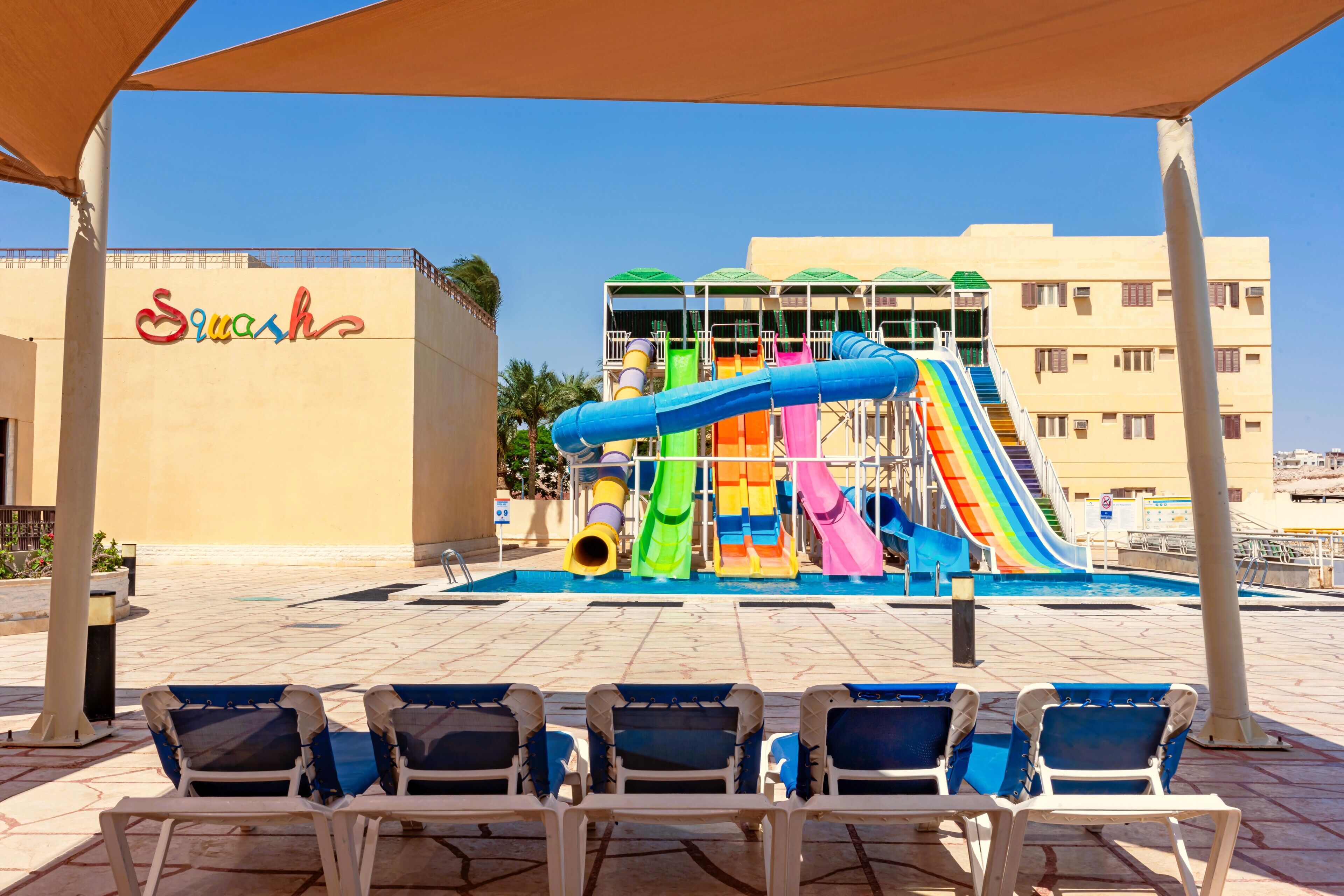 A pool area with a water slide, lounge chairs, and a building with a sign.