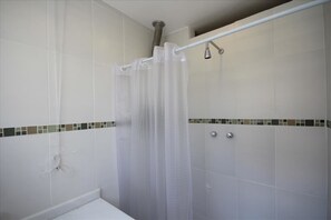 A shower area with a transparent curtain, tiled walls, and a metal showerhead. - GoHouse Copacabana 1005 A (Rio de Janeiro)