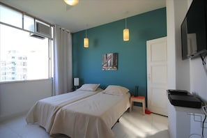 A bedroom with two beds, a window with curtains, a painting on the wall, and a desk with a keyboard. - GoHouse Copacabana 1005 A (Rio de Janeiro)