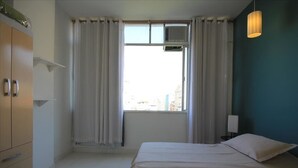 Een hotelkamer met een bed, een kledingkast, een raam met gordijnen, een wandairconditioner en een bedlamp.