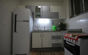 A compact kitchen with white cabinets, a refrigerator, a stove, and a sink.