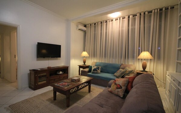 A living room with a flat-screen TV, a sofa, a coffee table, and two lamps.