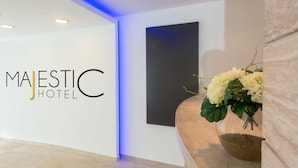A reception area with a modern design, featuring a reception desk, a wall-mounted sign for Majestic Hotel, and a decorative plant. - Majestic (Rhodes)