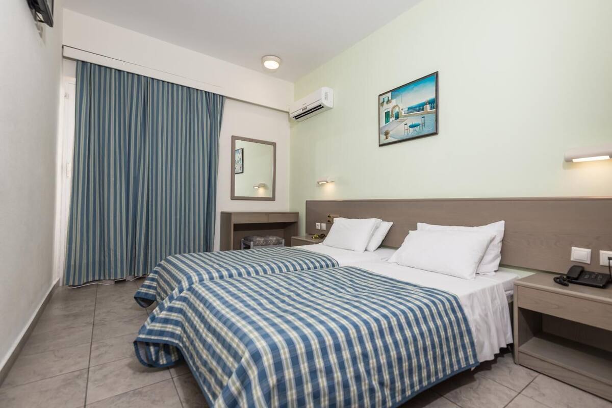 A hotel room with a large bed, a bedside table with a lamp, a small desk, and a window with curtains.