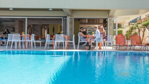 An outdoor pool area with white and orange chairs, a reception area, and a building entrance. - Majestic (Rhodes)