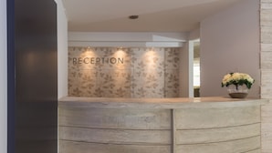 A reception desk with a 'RECEPTION' sign, a wooden design, and a vase with flowers. - Majestic (Rhodes)