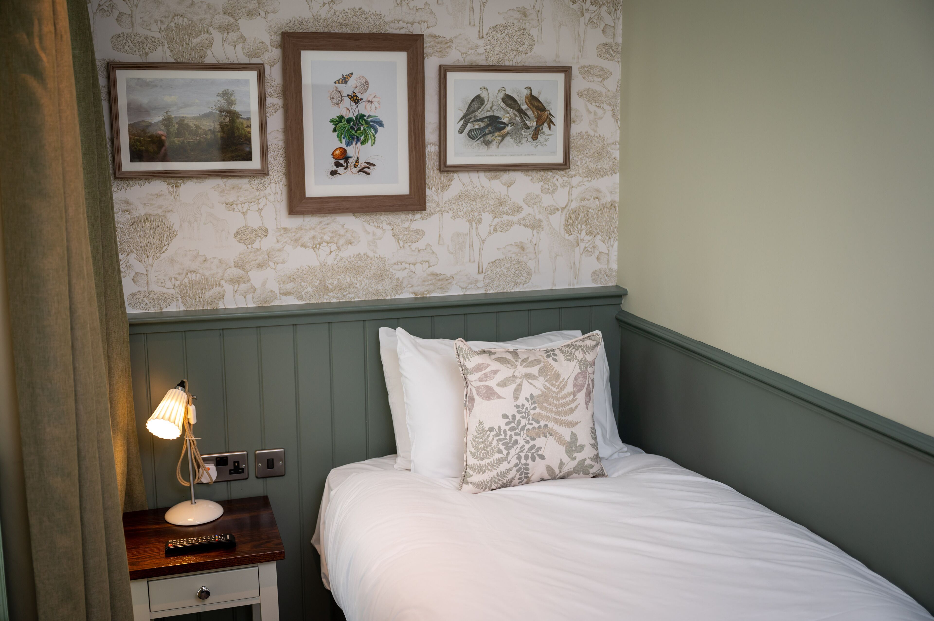 A bedroom with a bed, a nightstand with a lamp, and three framed pictures on the wall.