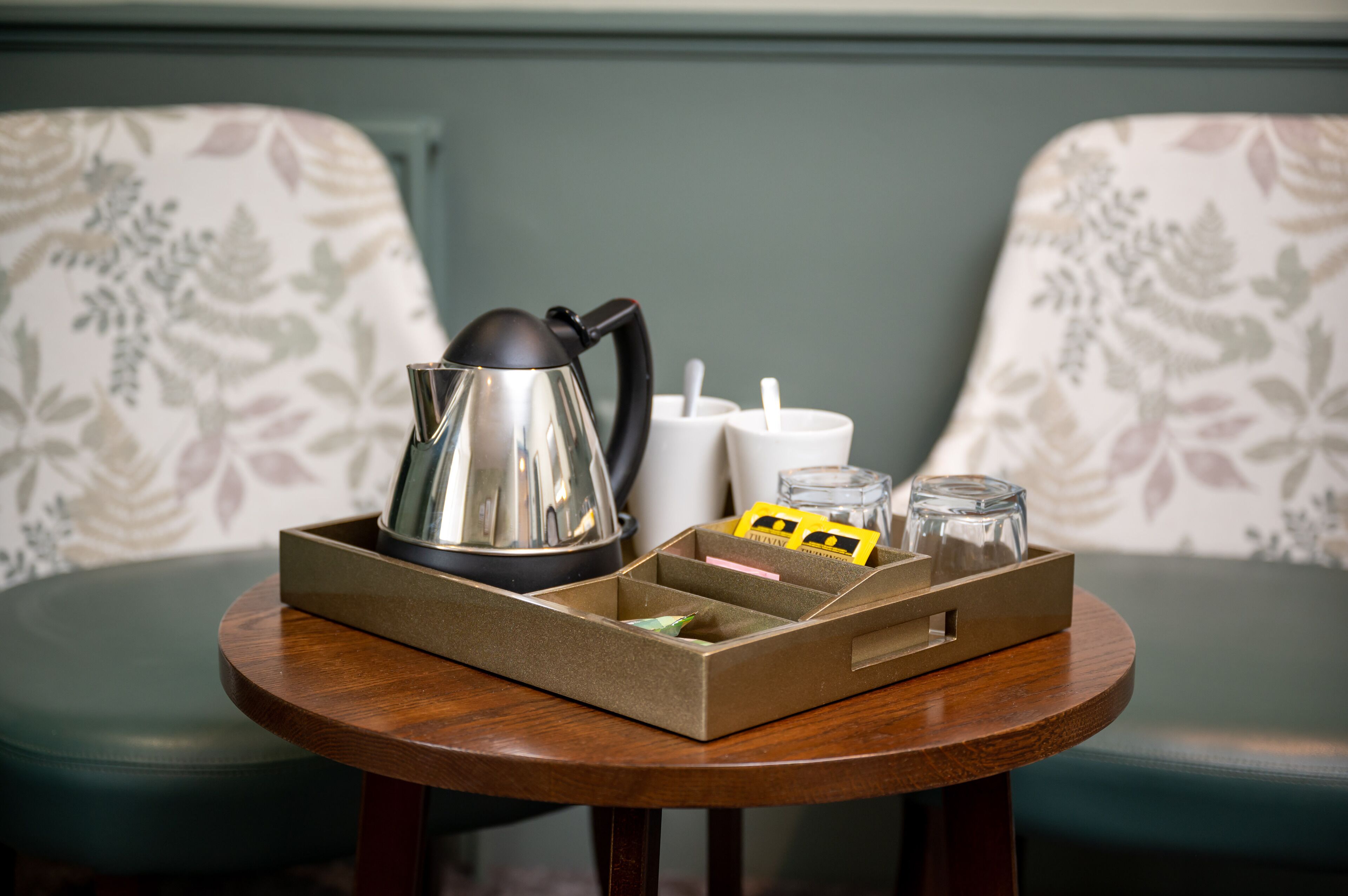 A small wooden table with a tray containing a kettle, a glass, and a box of tissues.