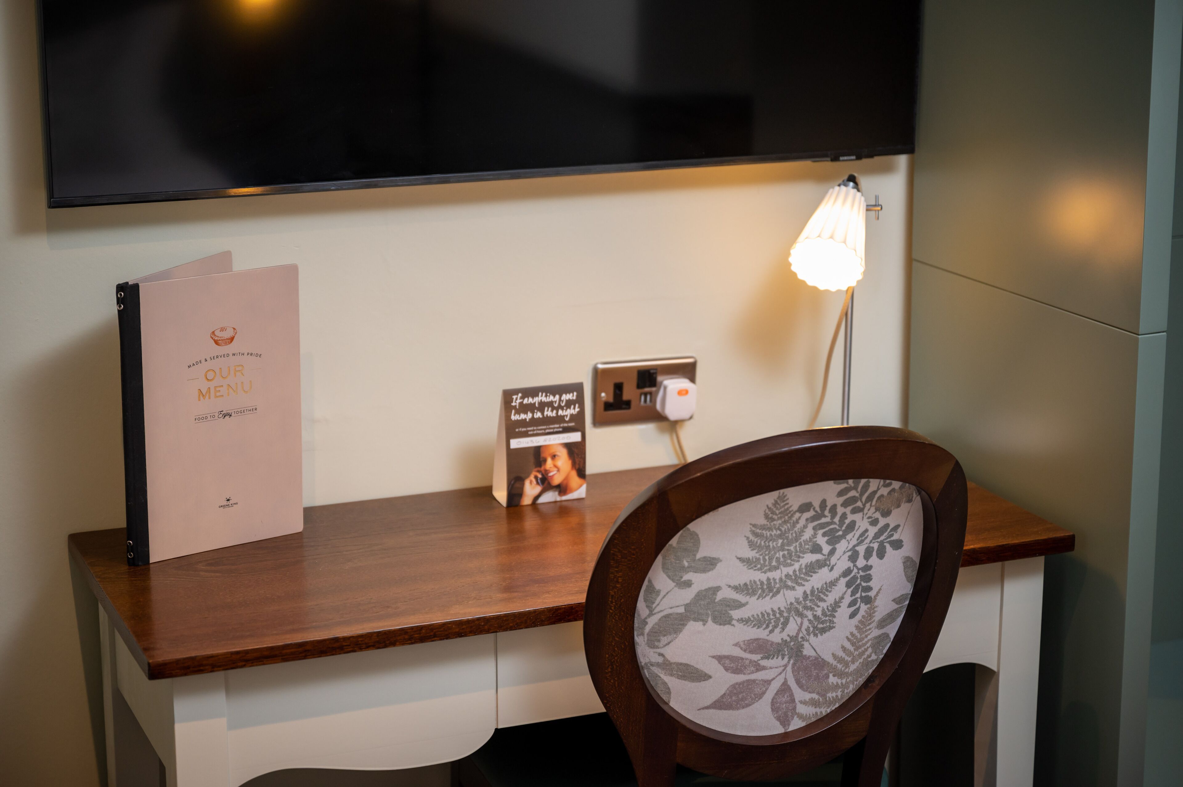 A wooden desk with a pink menu folder, a framed photo, and a lamp.