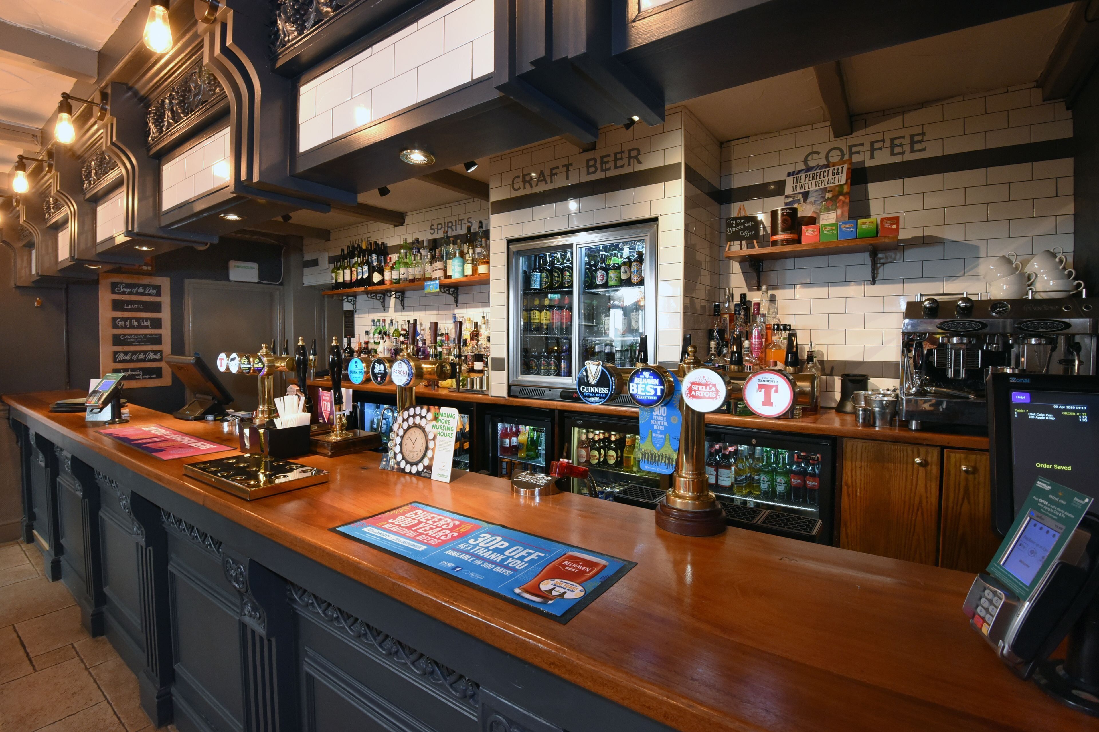 A bar area with a wooden counter, multiple beer taps, a coffee station, and a variety of liquor bottles.