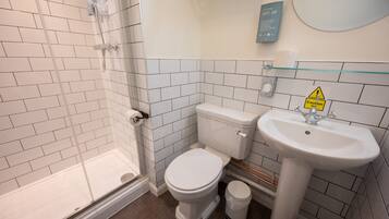 A bathroom with a glass shower enclosure, a white toilet, and a sink with a caution sign.