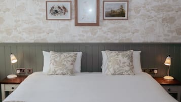 Una cama bien hecha con almohadas estampadas con motivos florales, dos lámparas de noche y una obra de arte enmarcada en la pared.