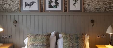 A neatly made bed with patterned pillows, a headboard with framed artwork, bedside lamps, and a textured wall behind.