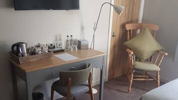 A hotel room with a bed, a desk with a chair, a television, and a wooden door.
