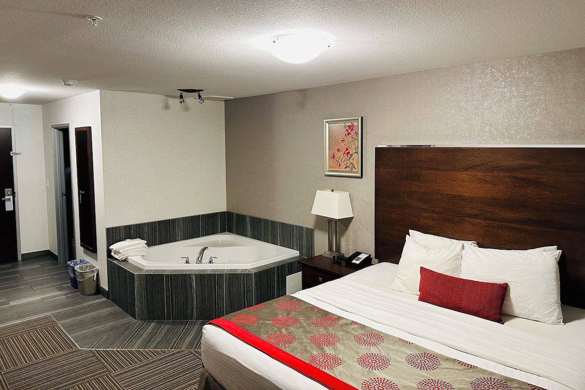 Une chambre d’hôtel avec un grand lit, une salle de bain séparée avec un jacuzzi et une tête de lit en bois.