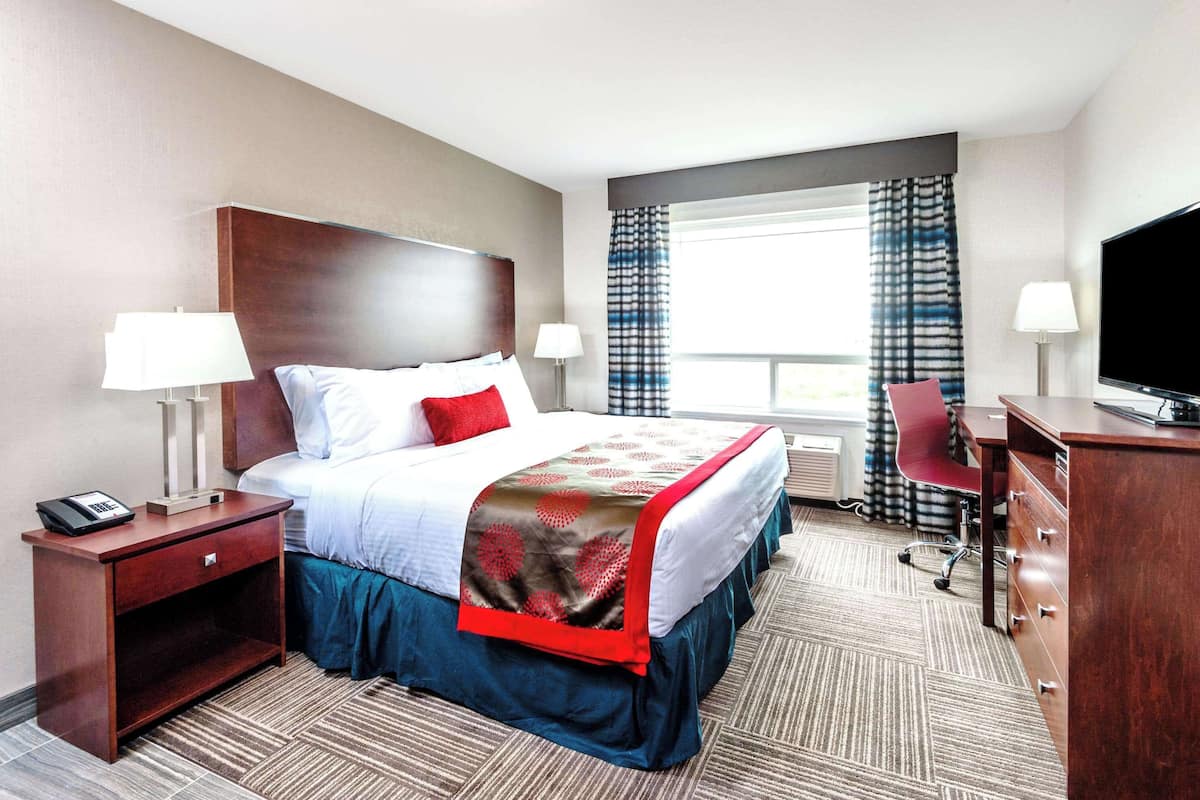 Une chambre d’hôtel avec un grand lit, deux tables de chevet, un bureau, une chaise, une télévision et une fenêtre avec des rideaux.