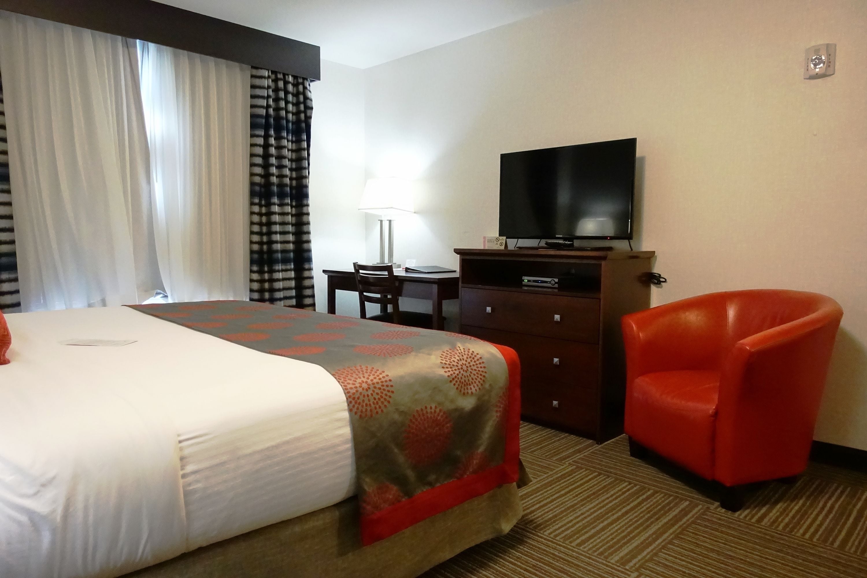 A hotel room with a bed, a desk, a television, and a red chair.