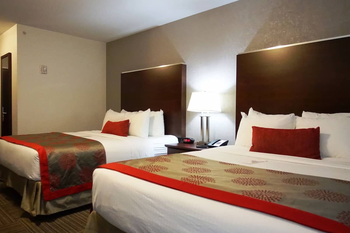 Une chambre d’hôtel avec deux lits, chacun recouvert d’une couverture rouge et beige, une table de chevet avec une lampe et un téléphone.