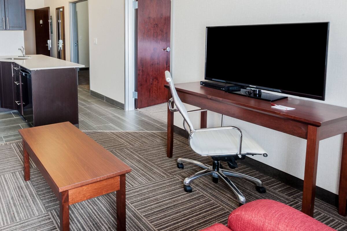 Une chambre d’hôtel avec un bureau en bois, une télévision, une chaise et une petite table.